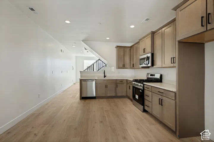 Kitchen featuring light-tone shaker cabinetry, solid-surface countertops, wood-finish flooring, recessed lighting, and stainless steel appliances