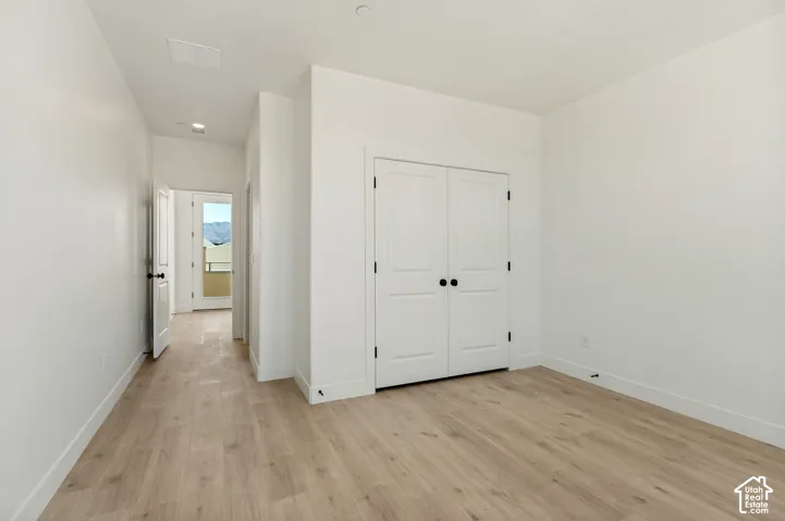 Interior room featuring wood-finish flooring, double-panel closet doors with matte black hardware, and crisp white wall finishes
