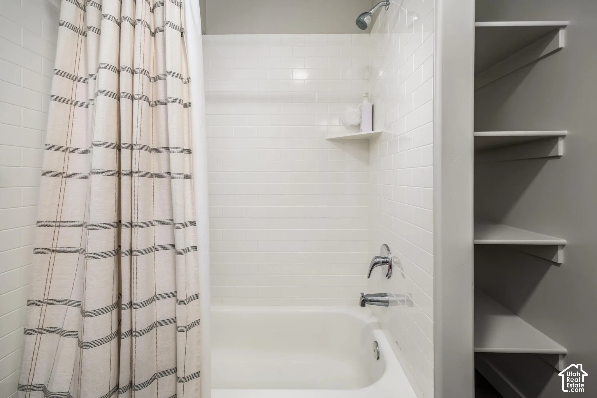 Shower-tub combination featuring subway tile surround, integrated corner shelving, chrome hardware, and built-in wall shelving