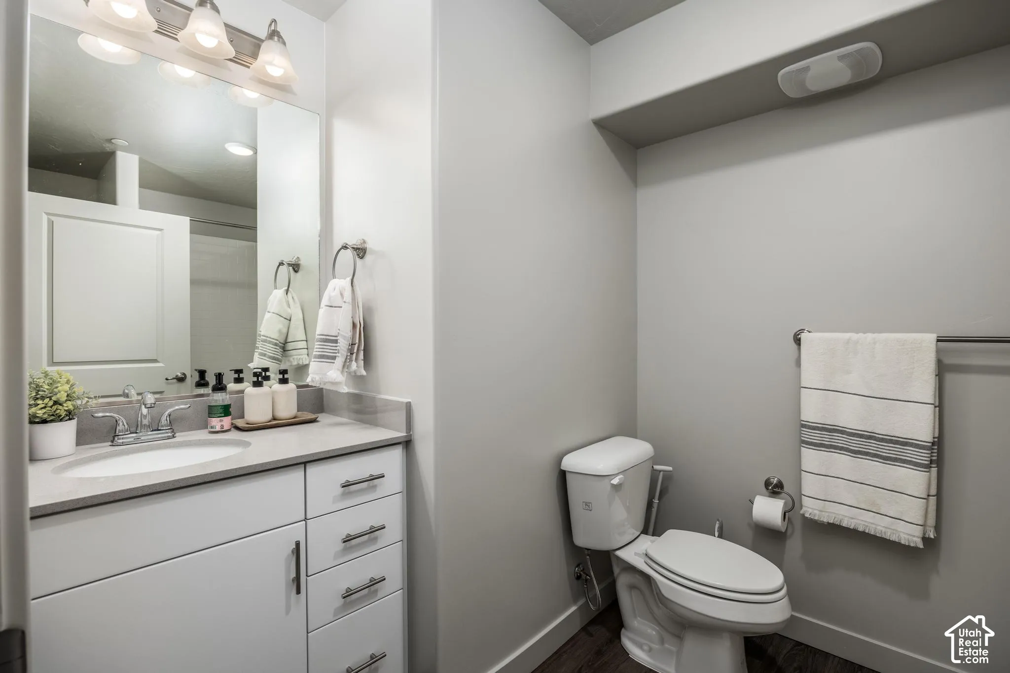 Bathroom featuring a white vanity cabinet with multi-drawer storage, a solid surface countertop with an integrated oval sink, a polished chrome faucet, a large vanity mirror, and wood-finish flooring