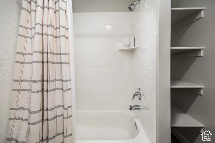 Shower-tub combination featuring subway tile surround, integrated corner shelving, chrome hardware, and built-in wall shelving