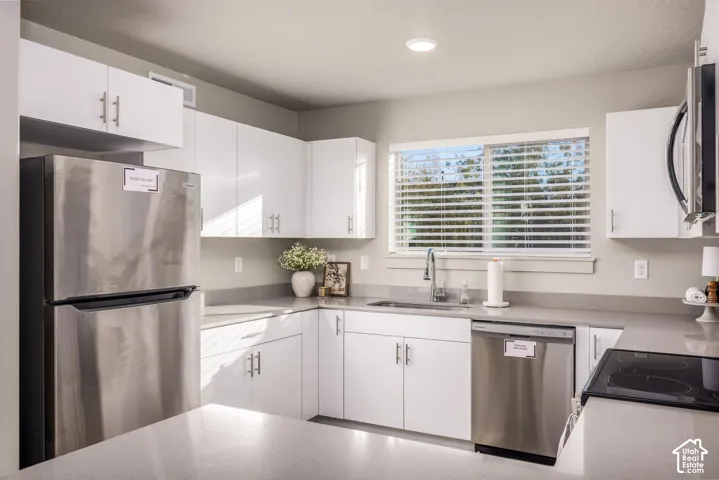 Kitchen featuring white slab-front cabinetry, neutral-toned solid surface countertops, stainless steel appliances, and a single-basin undermount sink with a gooseneck faucet