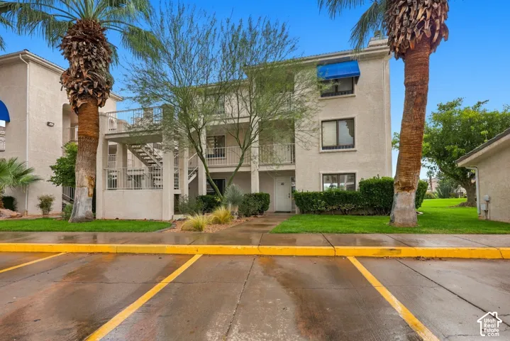 Multi-story stucco exterior featuring metal balcony railings, window awnings, and mature palm trees within landscaped grounds