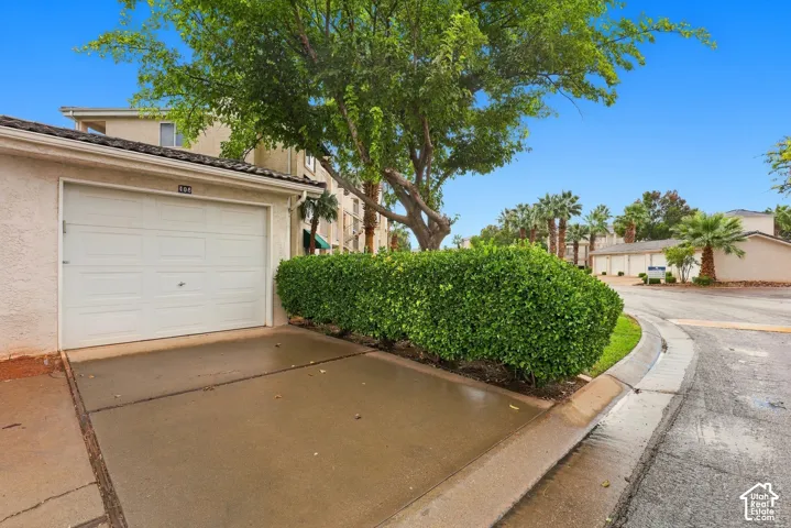 Single-car garage with a concrete apron, stucco exterior finish, and mature landscaping