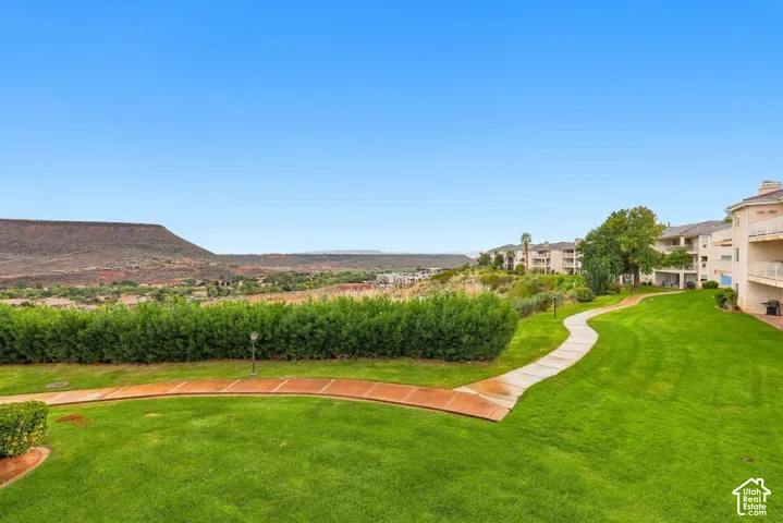 Expansive manicured lawn, curved concrete walkway, mature privacy hedges, and mountain range backdrop