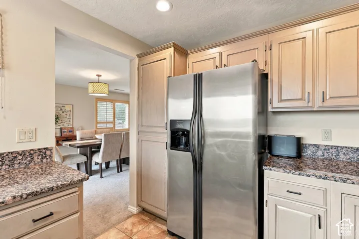 Kitchen featuring light-toned wood cabinetry, stone-patterned countertops, recessed ceiling lighting, and a stainless steel side-by-side refrigerator