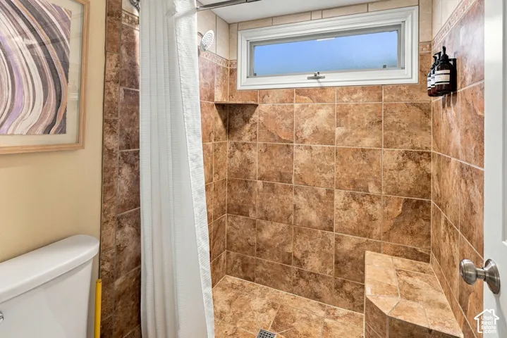 Shower enclosure featuring floor-to-ceiling stone-style ceramic tiling, a built-in tiled bench, a horizontal awning window, and an integrated corner shelf
