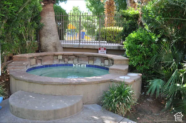 Spa featuring a stone-faced surround with concrete coping, integrated steps, and blue tile accents