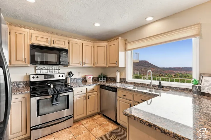Kitchen featuring light-finish cabinetry, stone-patterned countertops, stainless steel appliances, tile flooring, and a large window with mountain scenery
