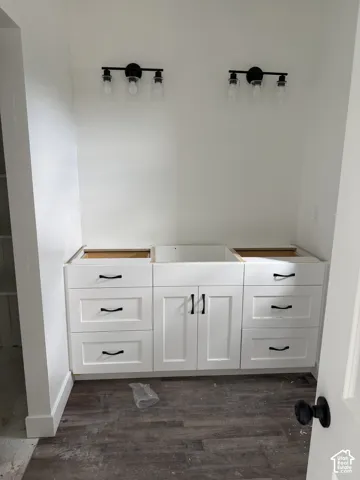 Custom white cabinetry vanity featuring recessed-panel drawers, center dual-door cabinet storage, dark hardware, and two triple-light wall-mounted fixtures over wood-finish flooring