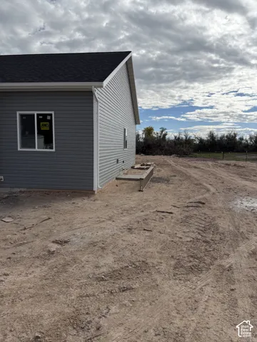 Exterior featuring horizontal vinyl siding, white trim, asphalt shingle roofing, and a concrete egress window well