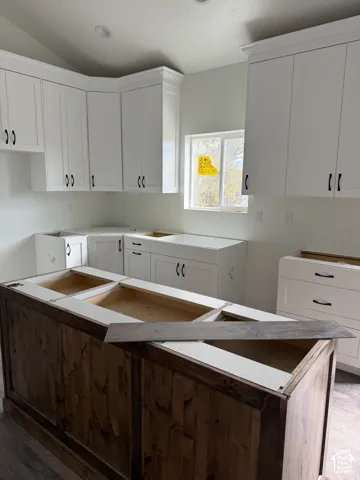 Kitchen featuring white shaker-style cabinetry, a central island with wood-finished paneling, recessed ceiling lighting, and a window providing natural light