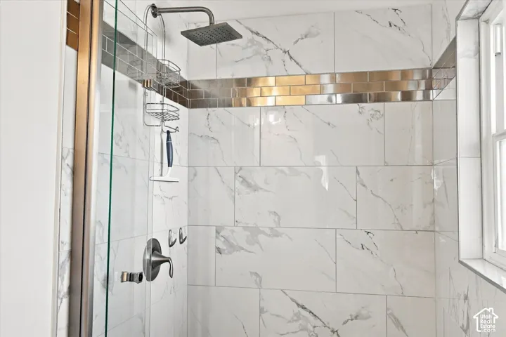 Walk-in shower featuring white large-format tile with grey veining, a metallic-finish accent tile border, a brushed-finish rainfall shower head, and a glass enclosure