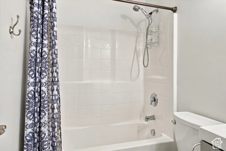 Bathtub with white tile-patterned surround, handheld shower fixture, polished chrome single-lever faucet, and wall-mounted metal coat hook