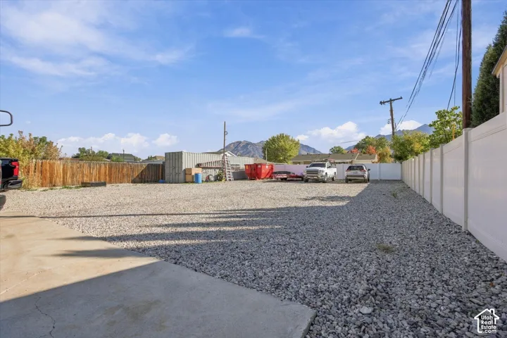 Gravel-surfaced exterior area featuring concrete paving, a white vinyl privacy fence, and a wood-slat fence perimeter with a mountain backdrop