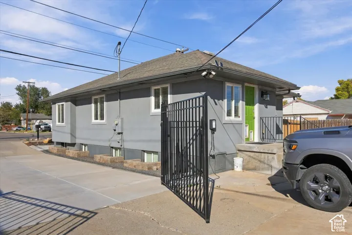 Grey stucco exterior with a hipped roof, concrete driveway, and black metal perimeter fencing