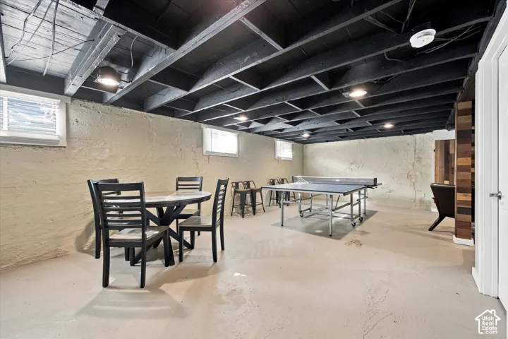 Open-concept space featuring exposed painted joist ceiling, recessed lighting, textured concrete walls, epoxy-finished flooring, and wood-paneled structural accent