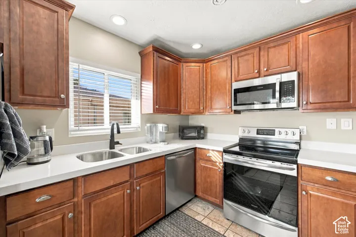 Kitchen featuring stained wood cabinetry, white quartz countertops, stainless steel appliances, a double-basin undermount sink with a matte black faucet, and recessed lighting