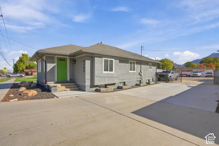 Stucco exterior featuring a hipped roof, concrete driveway, iron gate, and rock landscaping