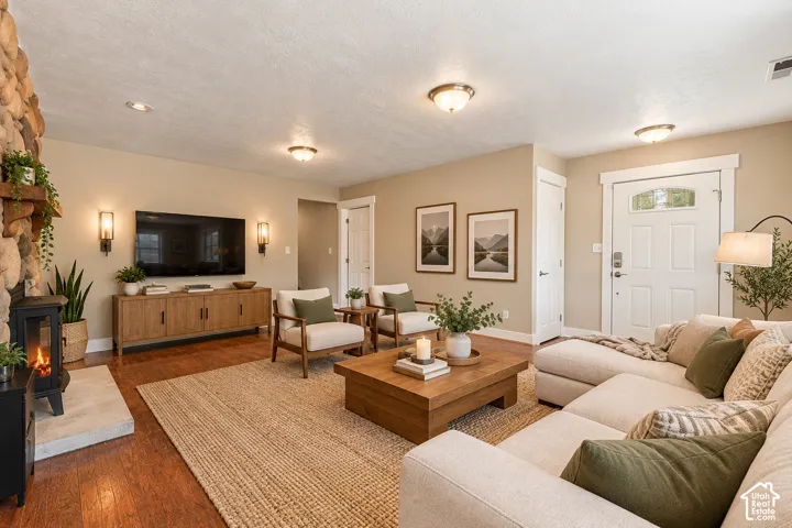 Interior space featuring wood-finish flooring, a stone-faced fireplace with a wood mantel, built-in wall-mounted light fixtures, and a white front door with an arched glass panel