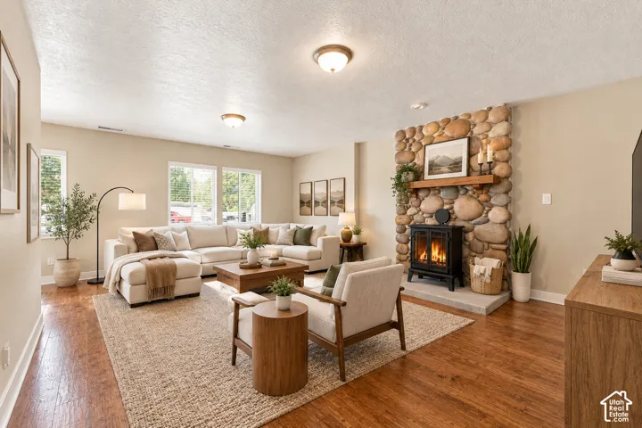 Floor-to-ceiling river rock fireplace with a wood mantel, black metal stove insert, wood-finish flooring, and recessed ceiling lighting