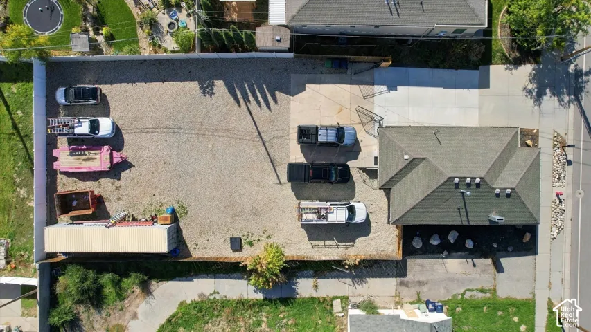 Aerial perspective of an expansive lot featuring a concrete driveway, gravel surfacing, perimeter fencing, and a detached metal storage structure