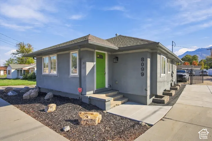 Single-story exterior featuring gray stucco siding, a hipped roof, a vibrant green entry door, and a concrete driveway