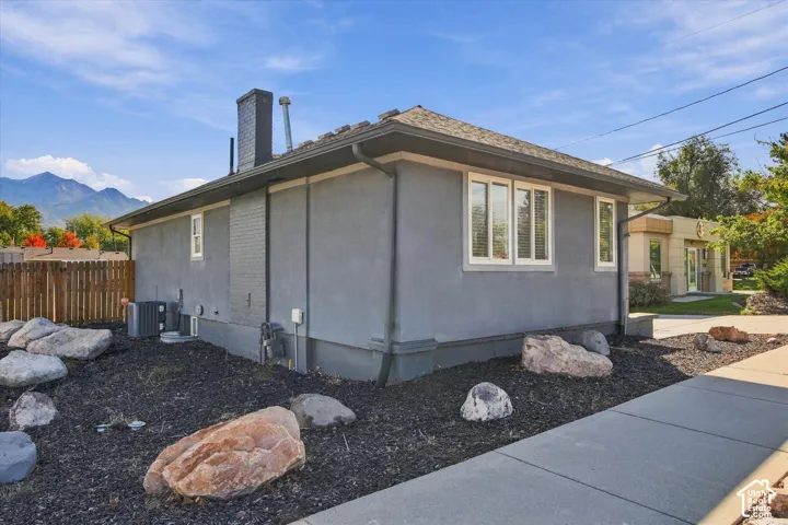 Stucco exterior featuring an external brick chimney, a pitched roofline, large-pane windows, and a landscaped rock garden