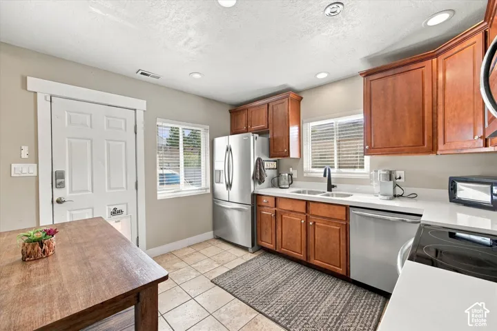 Kitchen featuring wood cabinetry, stainless steel appliances, white quartz countertops, dual-basin undermount sink with a matte black faucet, and ceramic tile flooring