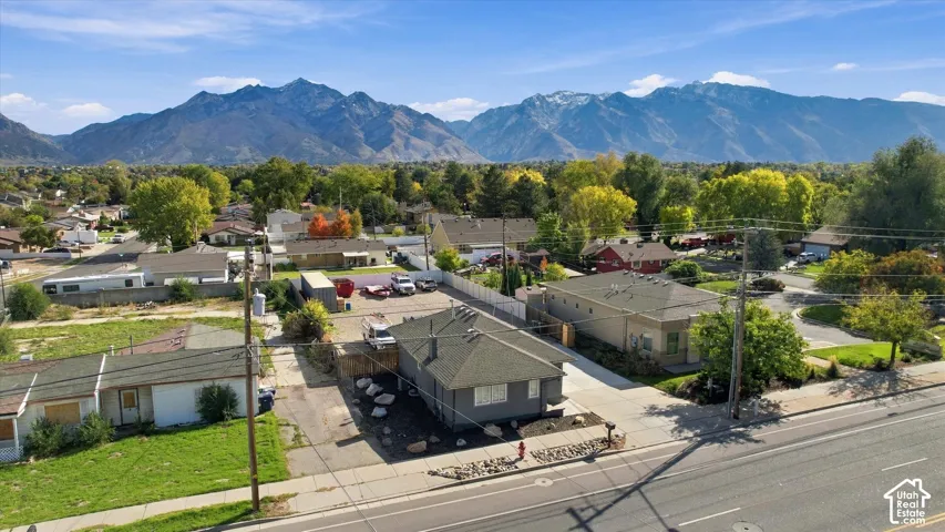 Aerial perspective featuring a single-story residence with a pitched shingle roof, asphalt driveway, stone landscape accents, and a mountainous backdrop