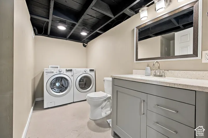 Grey shaker-style vanity with a solid surface countertop, rectangular undermount sink, framed mirror, and exposed ceiling joists