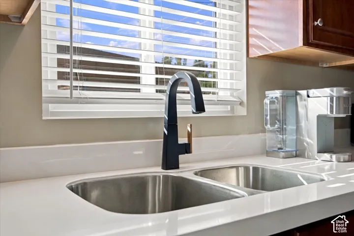 Dual-basin stainless steel sink featuring a matte black high-arc faucet with gold-tone accents, quartz countertops, and wood-finish cabinetry