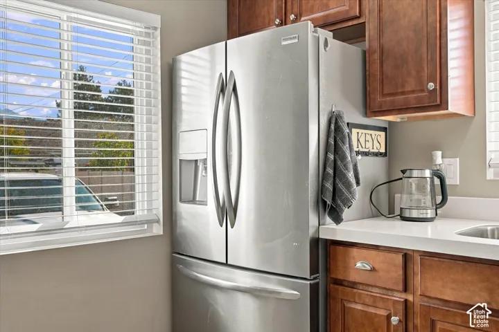 Stainless steel French door refrigerator, wood-finish cabinetry, quartz countertop, and horizontal slat window blinds