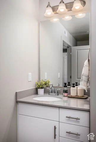 White vanity cabinet with brushed metal pulls, solid surface countertop, integrated undermount sink, polished chrome faucet, and multi-bulb wall-mounted lighting fixture