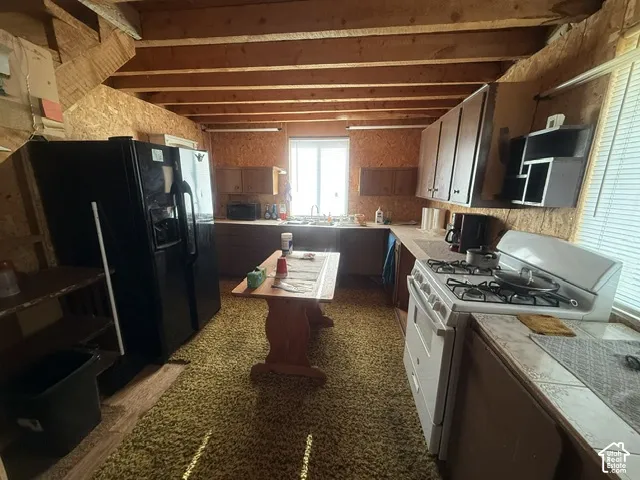 Kitchen featuring exposed wood ceiling beams, wood-composite wall panels, gas range, double-door refrigerator, and tiled countertops