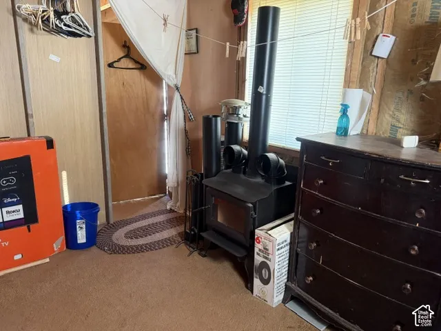 Cast iron wood-burning stove with vertical stovepipe and horizontal vent outlets, installed against an interior wall with windowed natural lighting