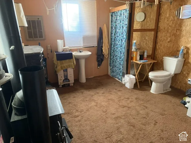 Bathroom featuring a pedestal sink, white porcelain toilet, wood-panel wall finish, and a black metal wood-burning stove
