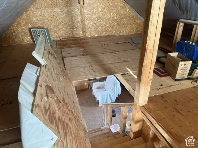 Unfinished attic space featuring exposed wood-framed rafters, plywood subflooring, and wooden stairs