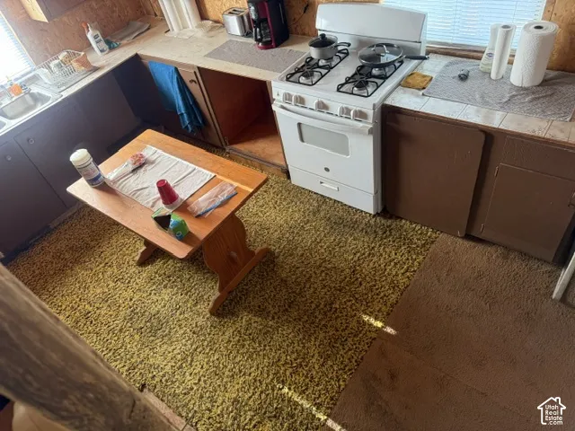 Kitchen featuring a free-standing gas range, stainless steel sink with a dual-handle faucet, and tile countertops