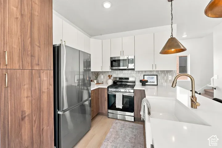 Two-tone cabinetry, stainless steel appliances, white countertops, textured backsplash, and a large single basin sink