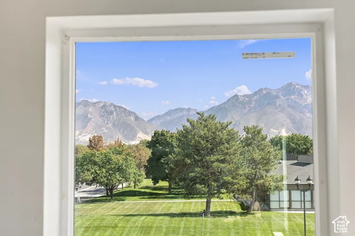 Framed window offering a mountain backdrop, mature trees, and a manicured lawn