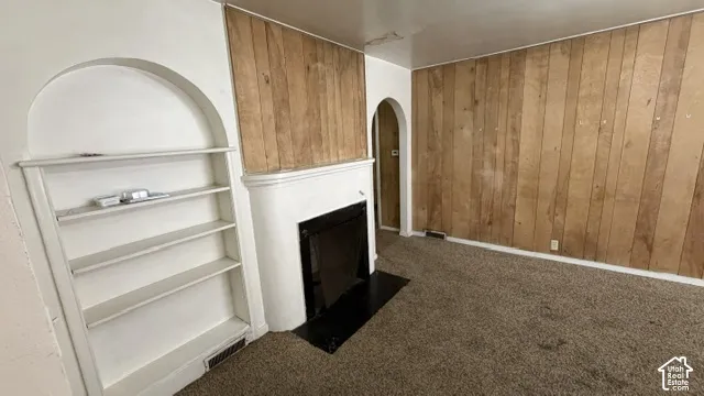 Fireplace featuring a rounded hearth, wood paneling, arched architectural detailing, and a built-in recessed shelving unit