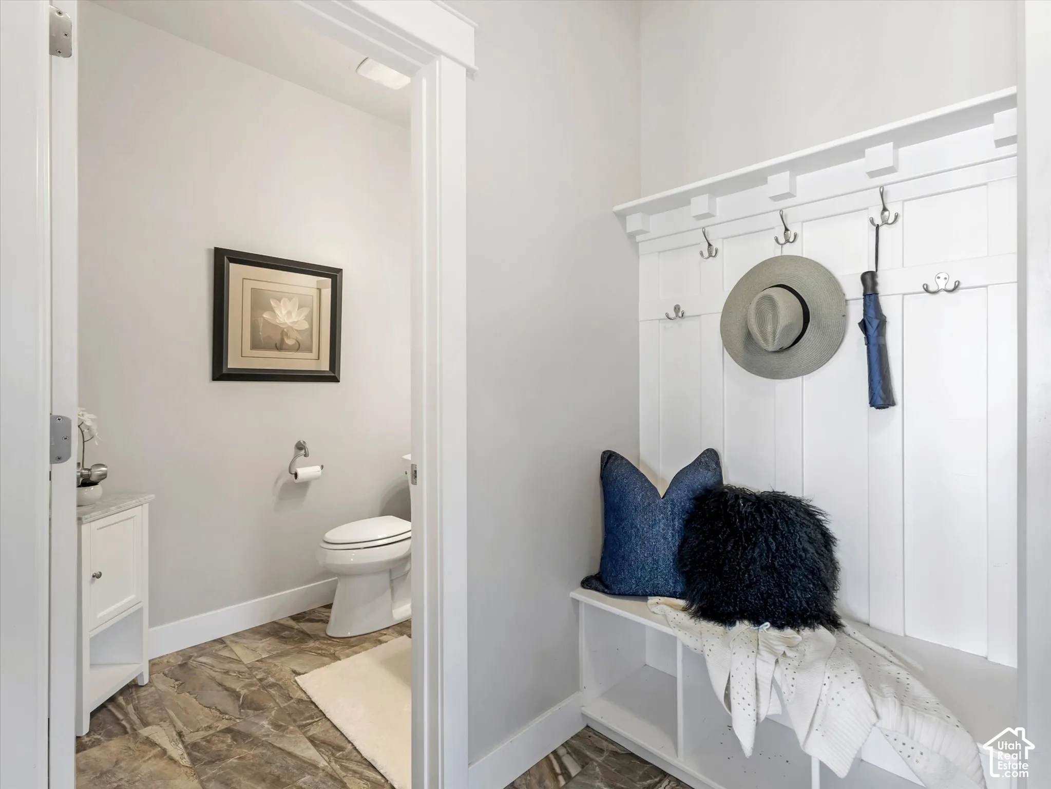 Built-in white mudroom bench with vertical board-and-batten detailing and integrated coat hooks, stone-finish flooring, vanity with stone countertop, and two-piece toilet