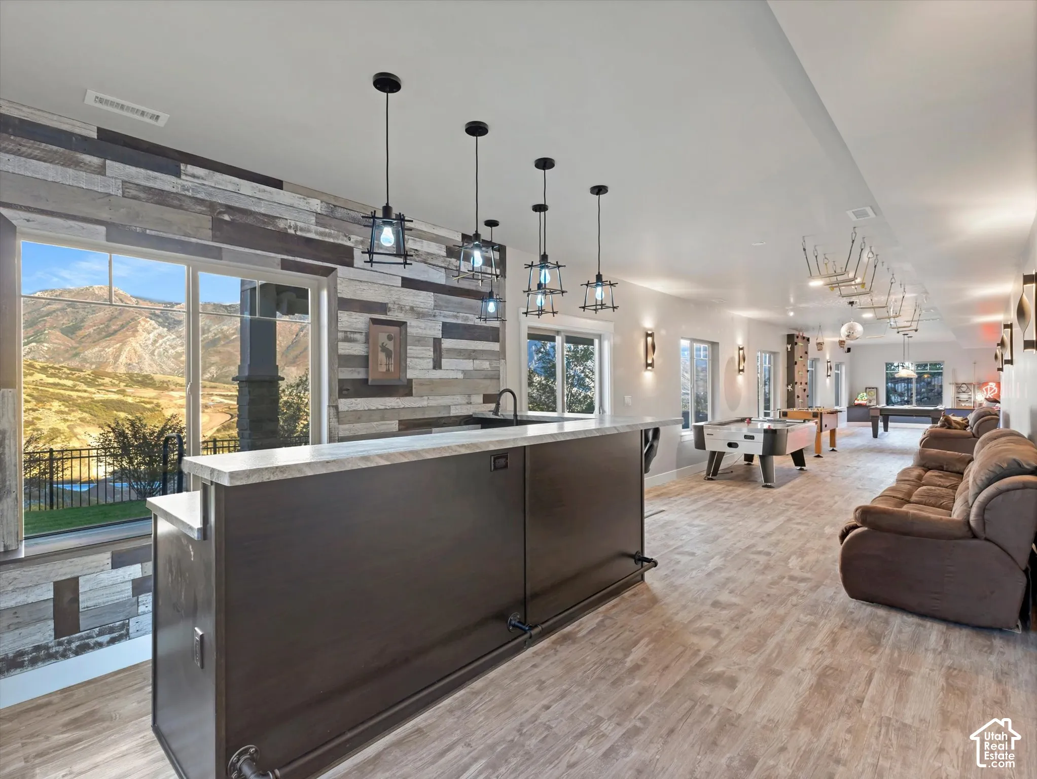 Built-in bar featuring a stone-patterned countertop, wood-finish cabinetry, industrial pendant lighting, reclaimed wood-style accent wall, and mountain backdrop