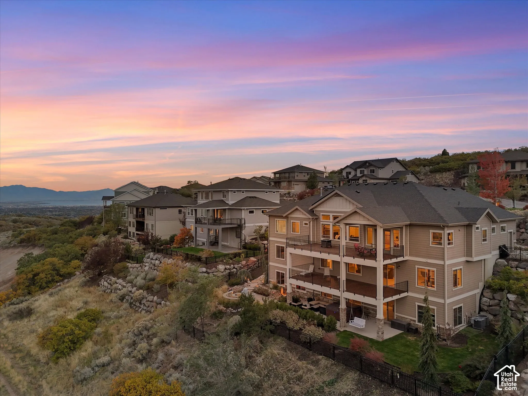 Multi-level residence featuring stacked rear decks, a covered ground-level patio, terraced rock landscaping, and mountain backdrop