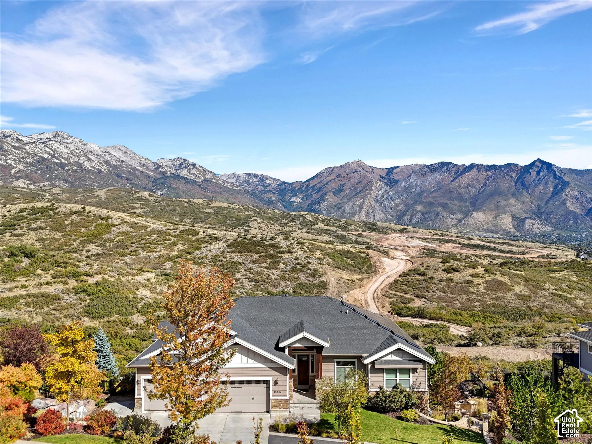 Multi-level residence featuring a dark shingle roof, horizontal siding, stone veneer accents, an attached multi-car garage, and a backdrop of mountain scenery