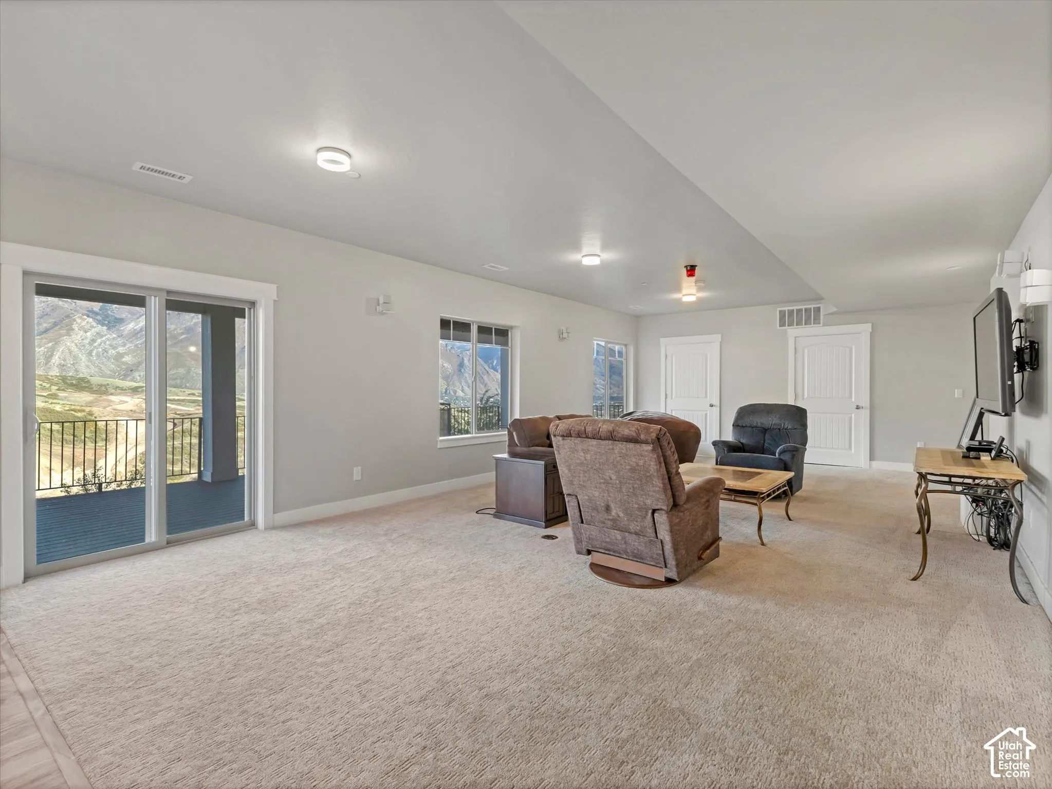 Neutral-toned interior space featuring recessed lighting, wall-to-wall carpeting, multiple windows, and a sliding glass door providing external access with mountain scenery