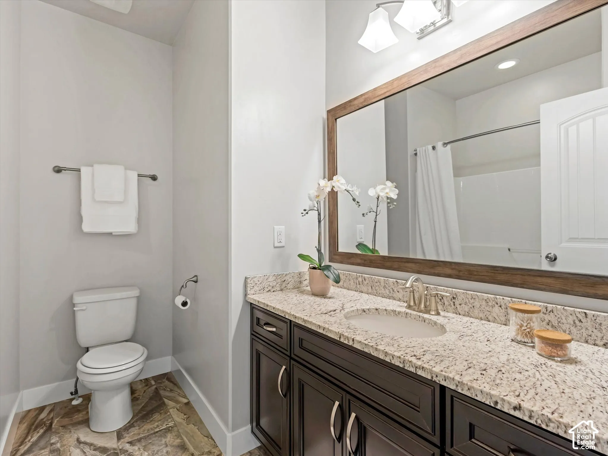 Bathroom featuring a dark wood vanity with stone-finish countertop, undermount sink, large framed mirror, and tile flooring