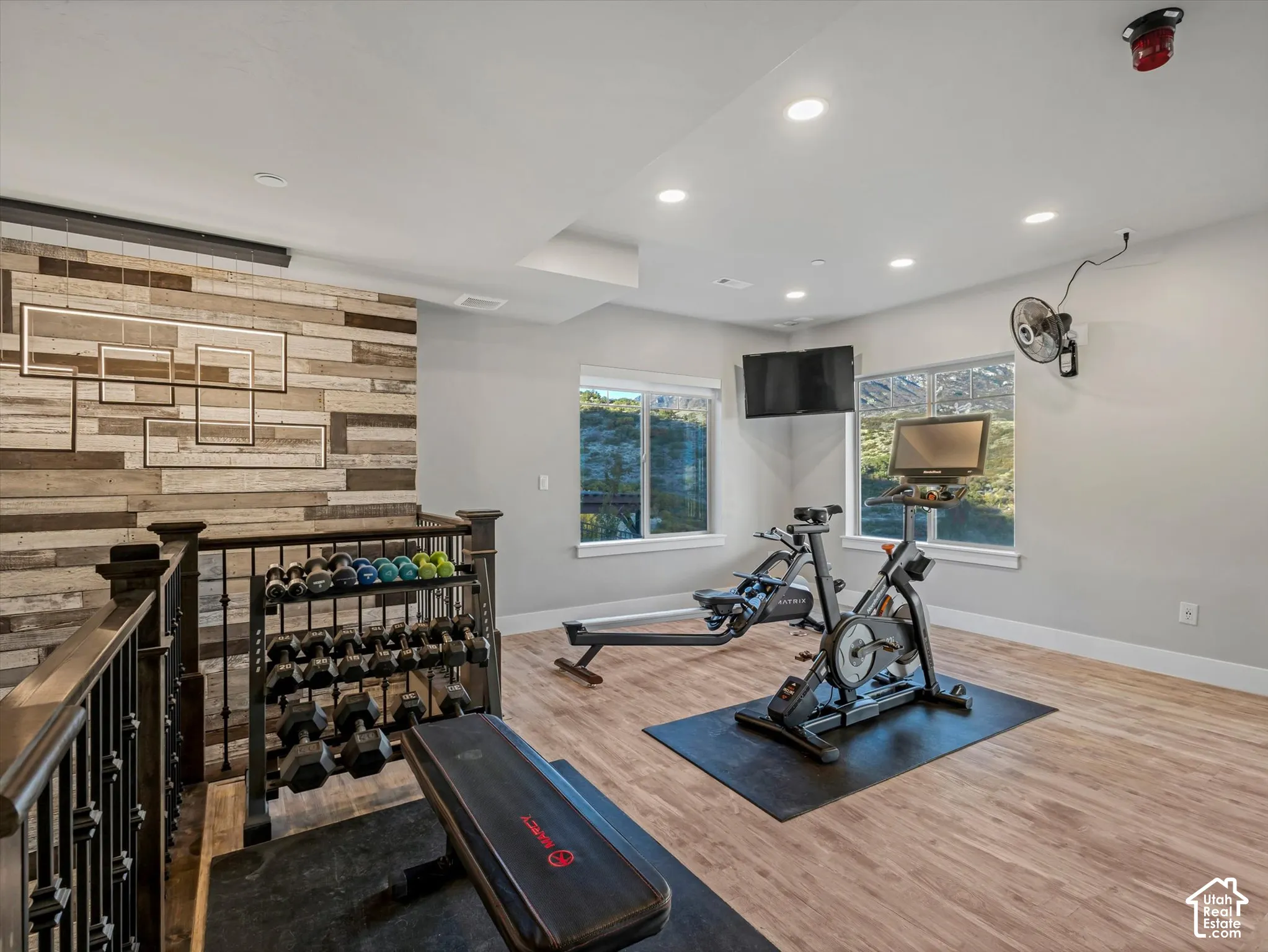 Recreation space featuring wood-finish flooring, recessed lighting, and a multi-textured wood-panel accent wall with integrated geometric lighting