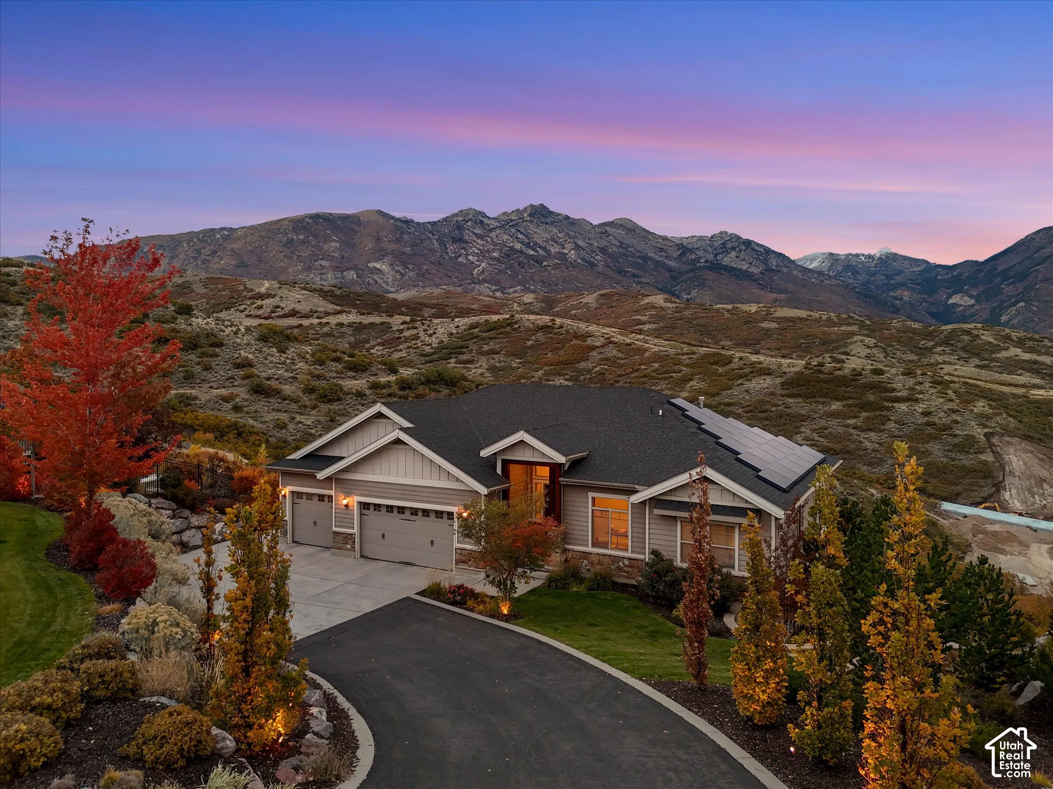 Single-level residence featuring a multi-car garage, asphalt driveway, solar panel array, and natural stone and siding exterior, all set against a prominent mountain backdrop